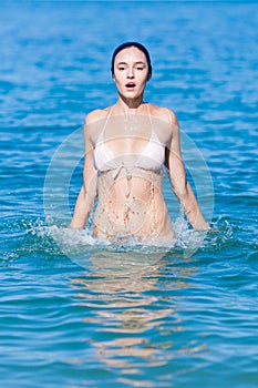 Wet young woman in bikini jumps out of water
