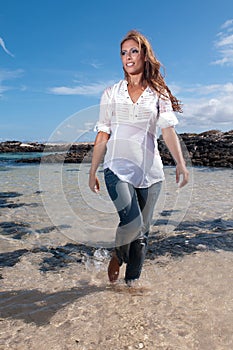 Wet young woman in clothes on the seashore in spring or summer