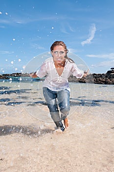 Wet young woman in clothes on the seashore in spring or summer