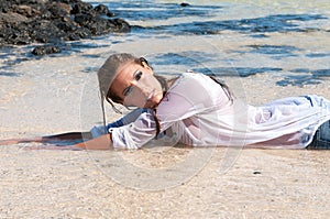 Wet young woman in clothes on the seashore in spring or summer