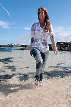 Wet young woman in clothes on the seashore in spring or summer