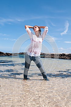 Wet young woman in clothes on the seashore in spring or summer