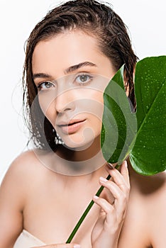 Wet young woman looking at camera with green palm leaf with water drops isolated on white