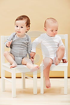 Weve got each other for fun. Adorable portrait of two cute babies sitting on chairs and smiling at the camera.