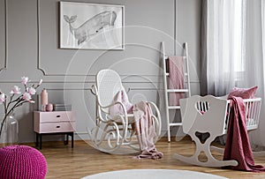 Whale poster on grey wall in child`s bedroom interior with rocking chair next to cradle. Real photo