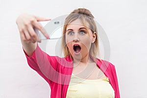 What?! Closeup portrait of unexpectedly attractive blogger woman in pink blouse standing, holding phone and making videocall with