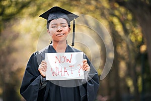 What do I do with my life now. Portrait of a young woman holding a sign that reads now what on graduation day.
