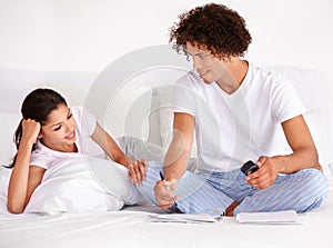 What do you feel like doing today. A happy young ethnic couple sitting on their bed writing something down.