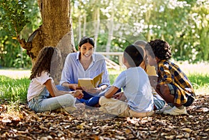 What fun activity should we do next. a teacher reading a book to her class in a park.