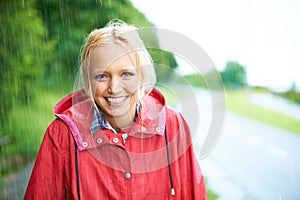 What a gorgeous smile. Gorgeous young blonde woman wearing a red raincoat in the rain outdoors on a country road.