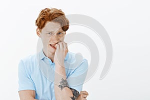 What if someone knows. Portrait of nervous intense unhappy male with red hair and freckles, frowning, biting fingernails