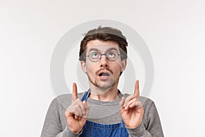 What is it. Intrigued and excited young surprised man in glasses and apron looking at something strange and curious