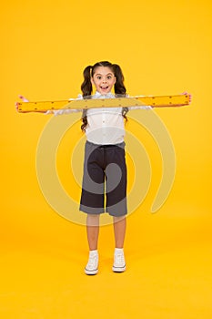 What a long ruler. Surprised little student holding rigid wooden ruler on yellow background. Small child taking