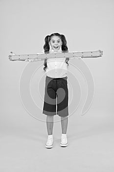 What a long ruler. Surprised little student holding rigid wooden ruler on yellow background. Small child taking