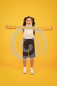 What a long ruler. Surprised little student holding rigid wooden ruler on yellow background. Small child taking