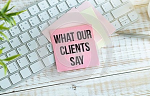 What Our Clients Say statement on paper note pad. Office desk with electronic devices and computer.