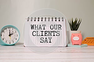 What Our Clients Say statement on paper note pad. Office desk with electronic devices and computer