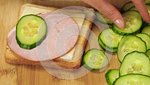 What's cookin. Sandwich close-up. The hand puts a slice of cheese, ham and vegetables on the bread. Fast food