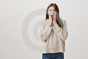 What shocking news. Good-looking amazed caucasian female in casual clothes standing with hands on face and dropped jaw