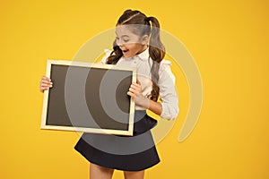 What is it. Surprised girl holding blackboard on yellow background. Little child preparing blackboard for lesson. Small