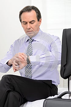 What time is it? Mature businessman looking at his watch while s