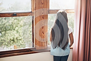 What waits for her in a great big world. Rearview shot of a young girl looking out of the window at home.