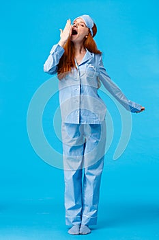 What wonderful morning. Full-length vertical studio shot yawning cute caucasian redhead girl in sleep mask and pyjama