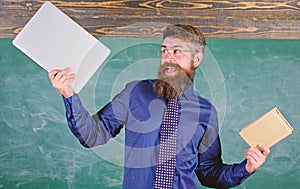 What would you prefer. Teacher bearded hipster holds book and laptop. Teacher choosing modern teaching approach. Paper