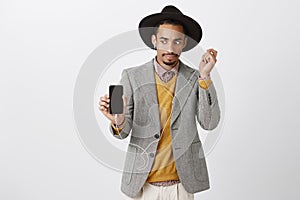 What is wrong with sound. Surprised worried handsome guy in trendy clothes and hat, showing smartphone to camera, taking