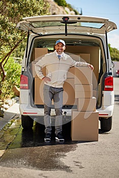 Whatever you are, be a good one. Portrait of a friendly delivery man unloading cardboard boxes from his van.