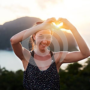 Whats there not to love about summer. Portrait of a young woman making a heart gesture outside.