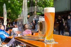 A wheat beer and a pils are standing on a table in a beer garden