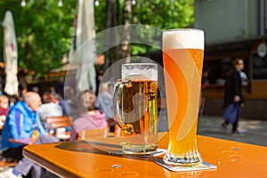A wheat beer and a pils are standing on a table in a beer garden
