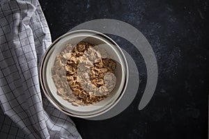 Wheat bran breakfast cereal with no milk in a bowl. Black background with homespun napkin