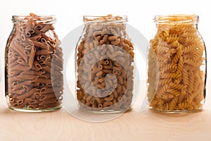 Wheat buckwheat and spelt pasta separated in three glass jars.
