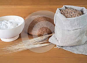 Wheat, ears, flour in a cup and bread on a wooden background