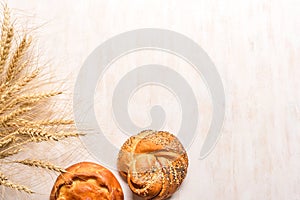 Wheat ears and fresh buns on white wooden background