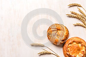 Wheat ears and fresh buns on white wooden background