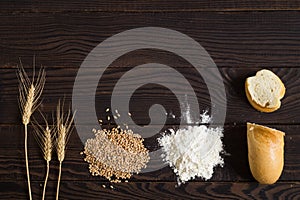 Wheat ears, grains, flour and sliced bread on a dark wooden table