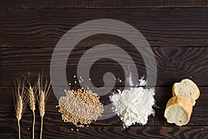 Wheat ears, grains, flour and sliced bread on a dark wooden table