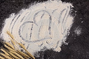 Wheat flour is scattered on a dark background. The ingredient. Bakery products. A heart is drawn on the flour