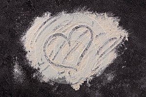 Wheat flour is scattered on a dark background. The ingredient. Bakery products. A heart is drawn on the flour