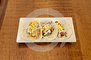 Wheat flour tortilla tacos with assorted fillings, grated cheese, pulled meat, sweet corn on wooden table