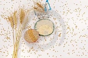 Wheat flour with wheat in bowl and wheat ears in shopping trolley isolated on white background