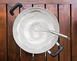 Wheat flour and whisk in the pan on wood background
