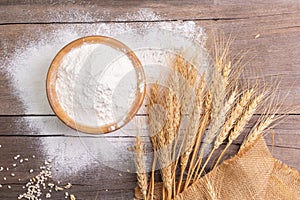 wheat flour in a wooden bowl There are ears of wheat on the table. Old wooden background - top view