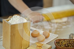 Wheat flour in wooden jar and eggs on oak kitchen table.