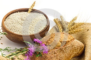 Wheat grains in wooden bowl, wheat ears and Wholemeal wheat flour in ceramic bowl, wheat ears, homemade bread and cornflowers