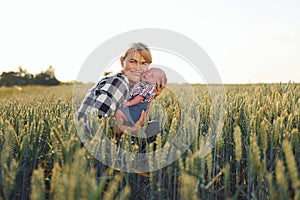 In the wheat. Happy woman on the agricultural field is with little baby in the hands