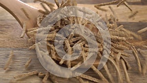 Wheat rye bran flakes sticks fall on a wooden spoon in slow motion. On a rustic wood surface